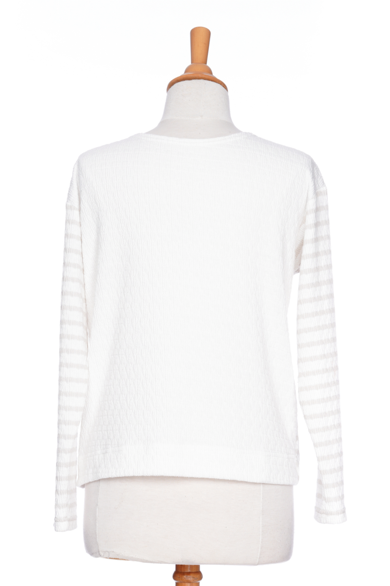 The Collins Reversible Sweater by Rien ne se Perd in Sand/White is shown on a mannequin agains ta white background. t's reversible back to front with stripes on side and solid fabric on the other. It has long striped sleeves and a round neck. 