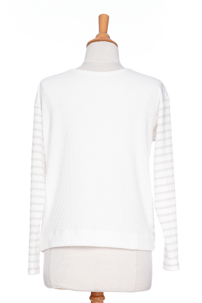 The Collins Reversible Sweater by Rien ne se Perd in Sand/White is shown on a mannequin agains ta white background. t's reversible back to front with stripes on side and solid fabric on the other. It has long striped sleeves and a round neck. 