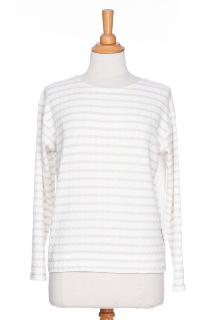 The Collins Reversible Sweater by Rien ne se Perd in Sand/White is shown on a mannequin agains ta white background. t's reversible back to front with stripes on side and solid fabric on the other. It has long striped sleeves and a round neck. 