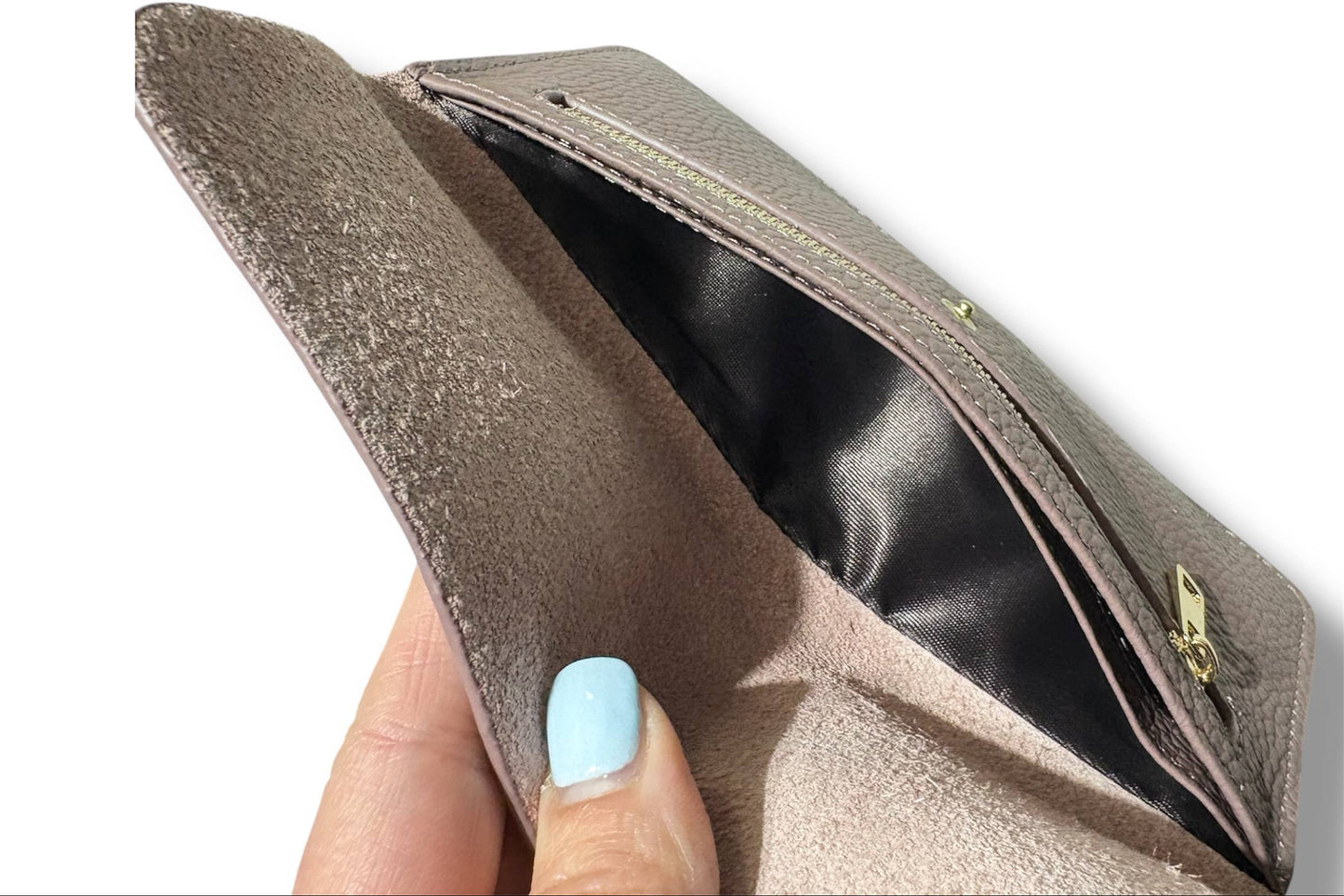 A close-up of a taupe pebbled leather wallet from Armoir being held open by a hand with light blue nail polish, showing a suede-like interior lining and a gold zipper.