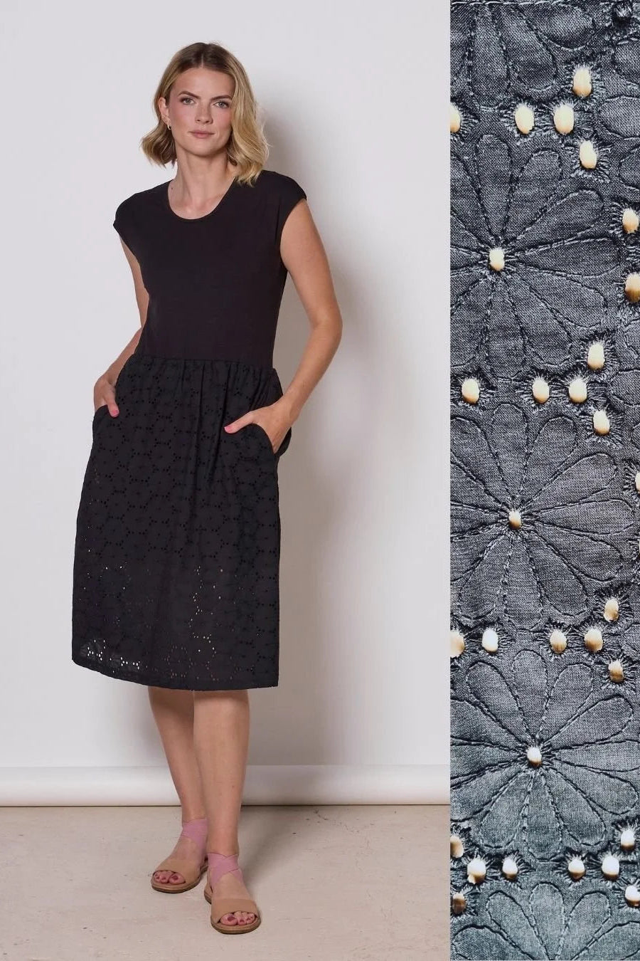 A woman wearing the Primrose Dress by Tangente in Black, a below the knee length dress featuring a bamboo rayon bodice and daisy eyelet skirt, with short sleeves and a round neck, standing against a plain background. A swatch of the eyelet fabric is shown next to the photo. 