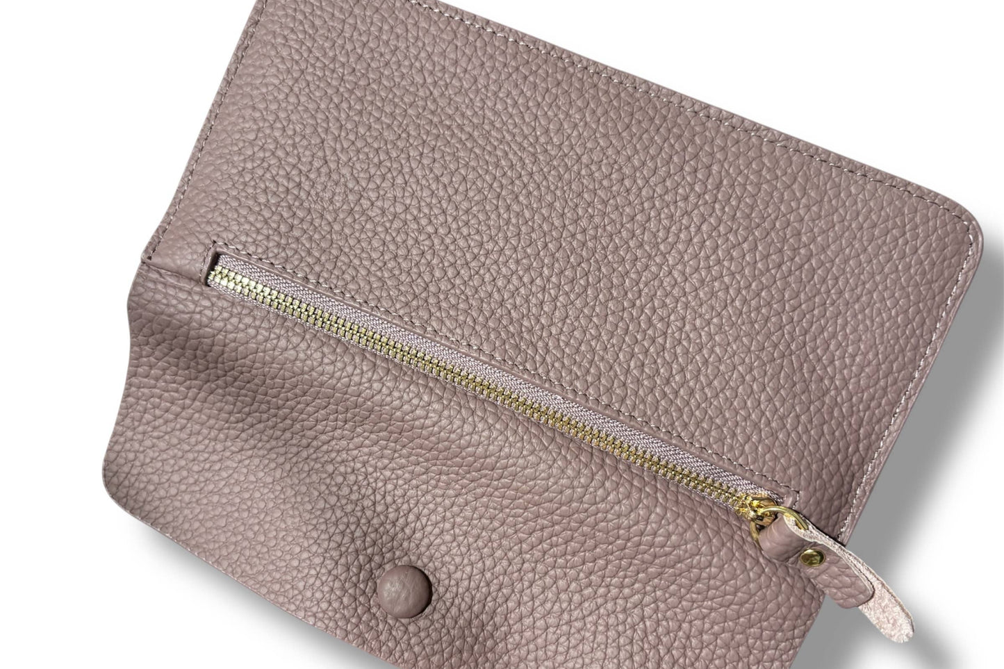 A close-up of a taupe pebbled leather wallet from Armoir showing a suede-like interior lining and a gold zipper.