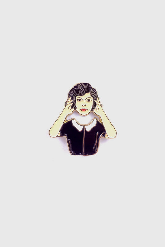 The Floating Head Pin by Badaboöm Studio, an enamel pin showing a woman lifting her head over her shoulders, is shown against a white background. 