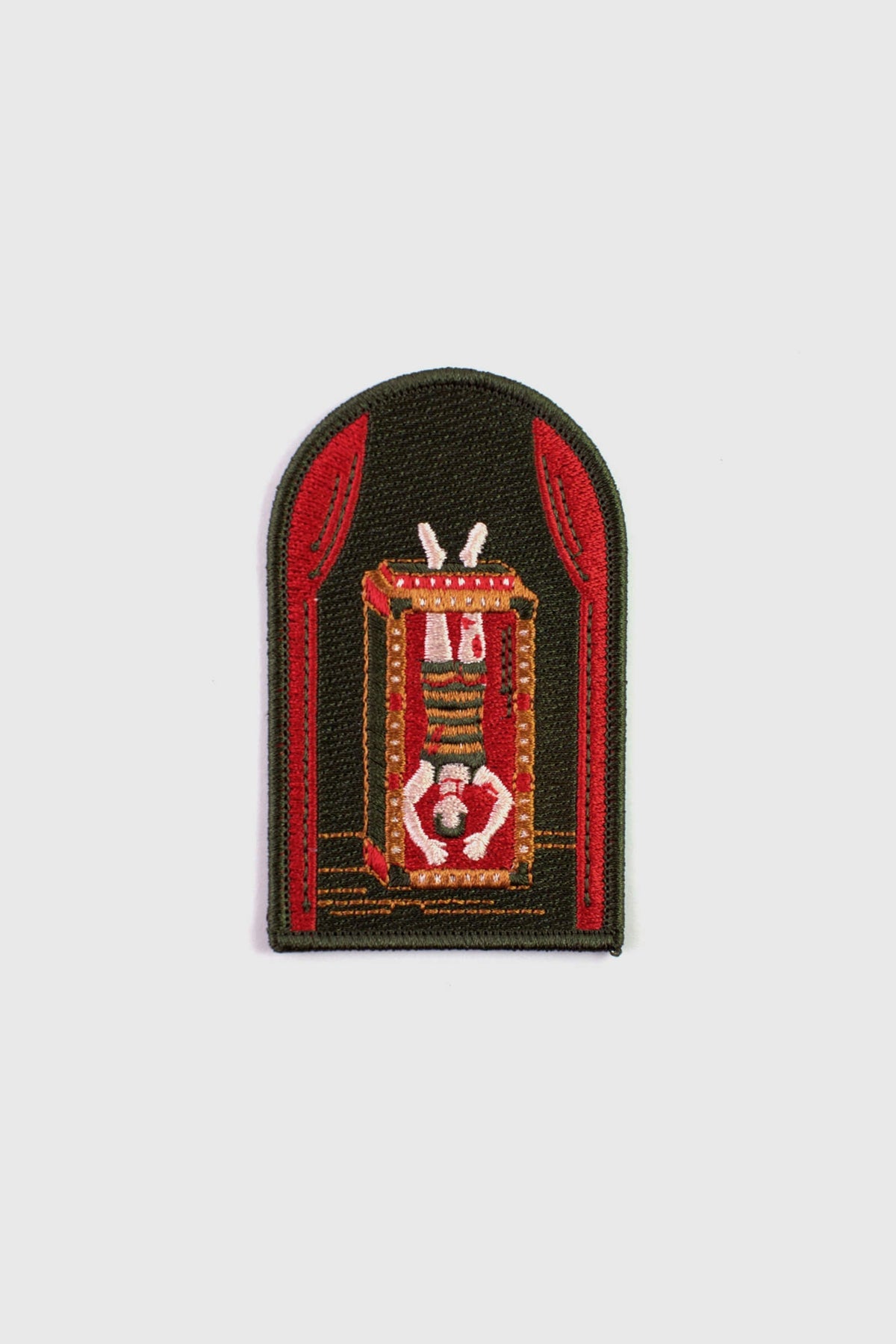 An embroidered arched patch from Badaboöm Studio showing Houdini upside down in a water tank. 
