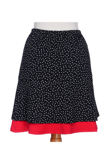 A back view the Sambuca Skirt from Rien ne se Perd in black and white polka dots with a Red peekaboo ruffle. It has an elastic waist and an A-line shape that hits above the knee. 