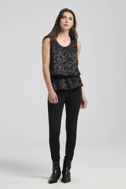 A woman wearing the Ella Pants from Kollontai in Black, slim pants with a wide pull on waistband. She's wearing them with a black patterned tank top against a white background