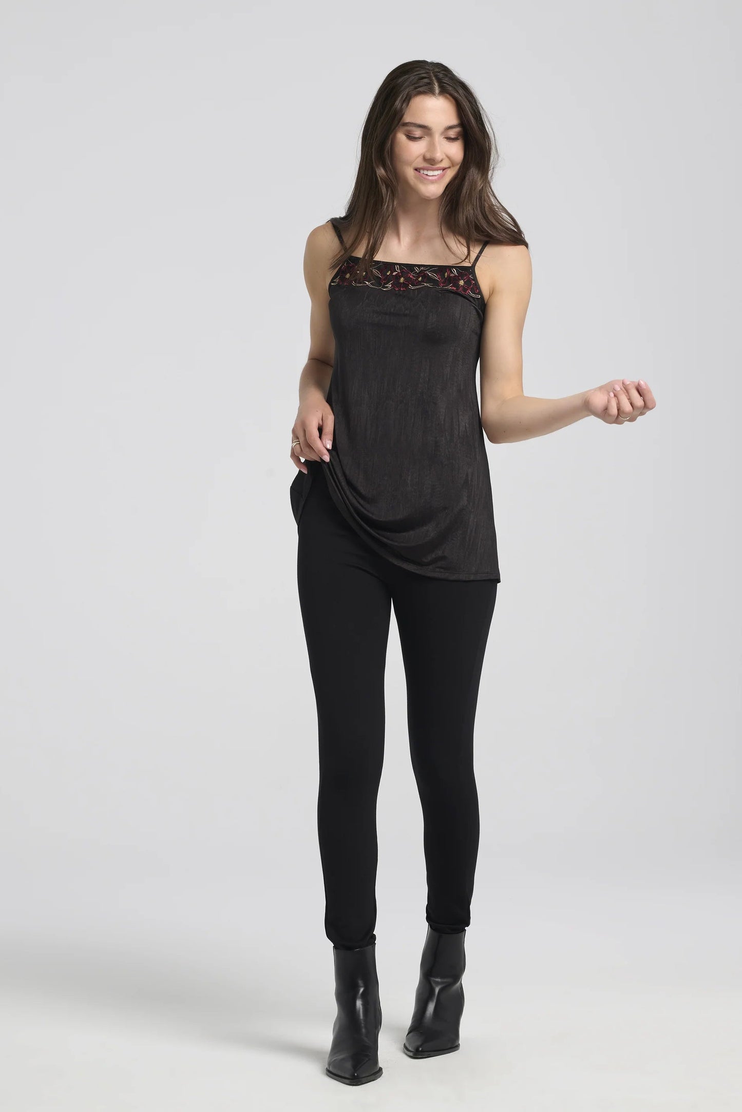 A woman wearing the Ella Pants from Kollontai in Black, slim pants with a wide pull on waistband. She's wearing them with a black  tank dress against a white background