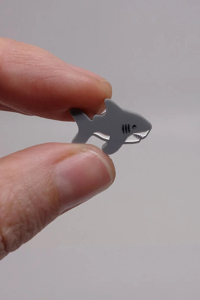 Hand holding Lilipop's shark-shaped earring against a plain background