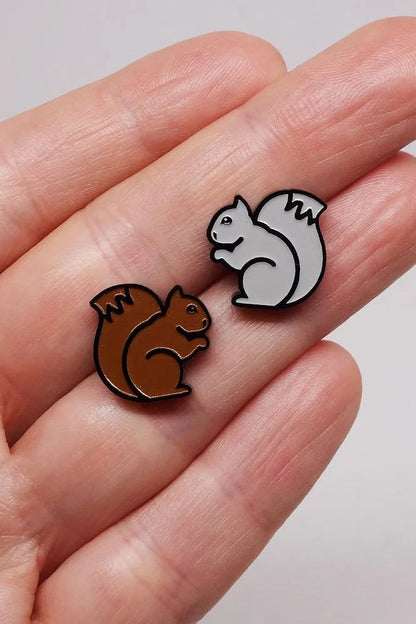 Two Lillipop squirrel-shaped earrings held between fingers against a neutral background
