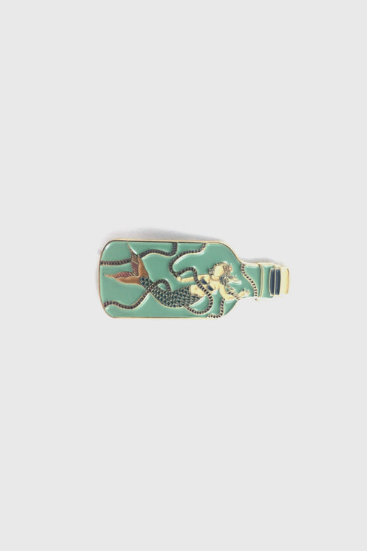 The Mermaid in a Bottle Pin from Badaboöm Studio, an enamel pin featuring a mermaid trapped in a light green bottle, is shown against a white background. 