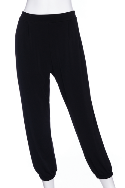 The Pina 7/8 Pants by Rien ne se Perd in Black, with a pull on waist, front pleats, cuffed legs, and a pockets, are shown on a mannequin in front of a white background. 