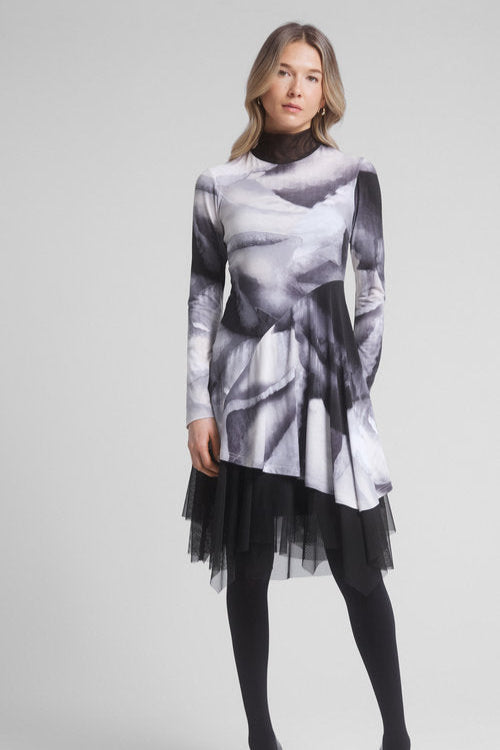 A woman wearing the Joe Tunic by Dinh Ba in Grey, an asymmetrical tunic in a swirl pattern with a contrasting black mesh turtleneck and long sleeves. 