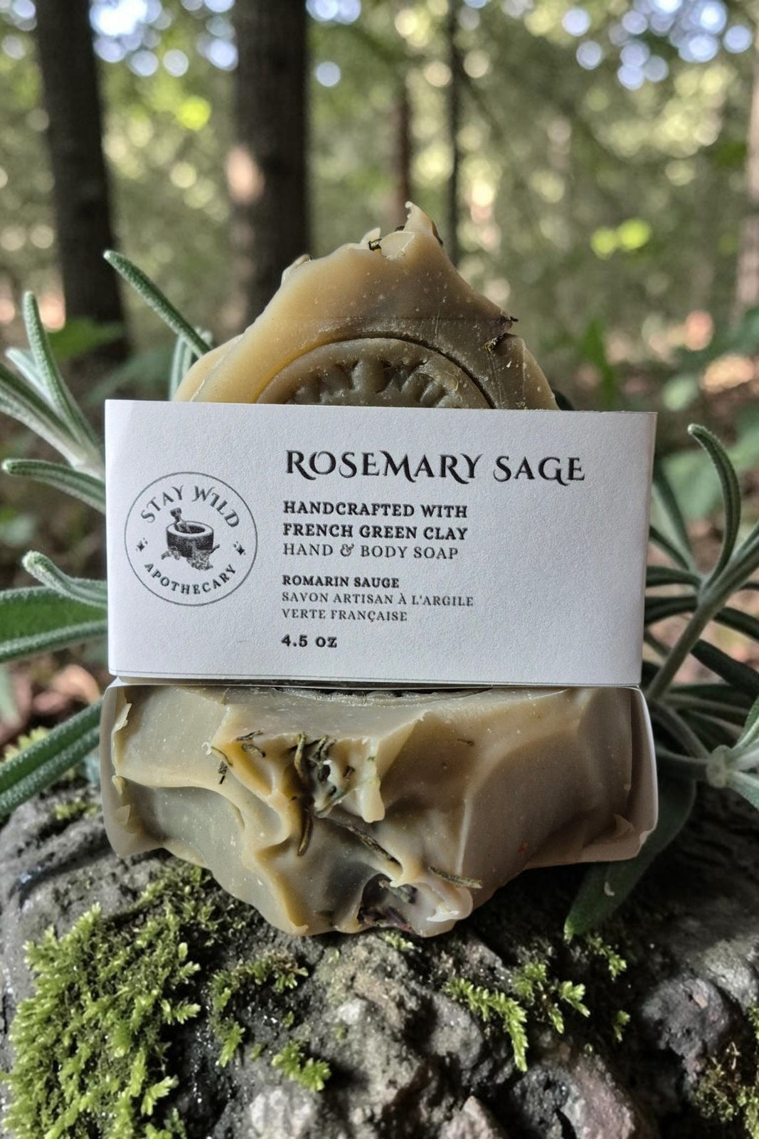 A bar Rosemary Sage Soap by Stay Wild Apothecary pictured atop a mossy rock in a forest setting 