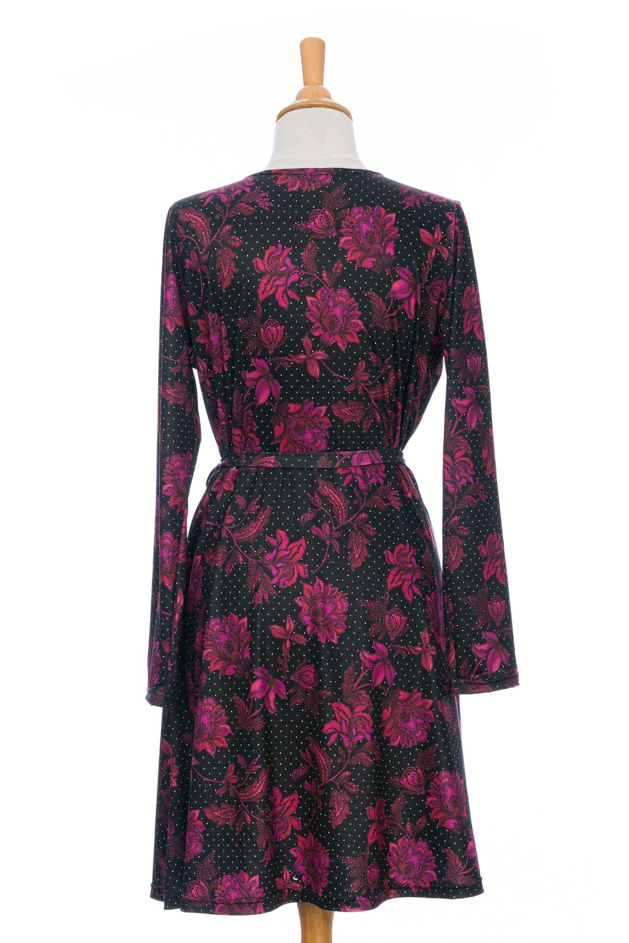 A back view of the Epilobe Dress by Rien ne se Perd in Polka Dots and Roses, a classic wrap dress with a tie at the waist, delicate pleats at the shoulders, and a hem that hits above the knee, is shown on a mannequin in front of a white background. 