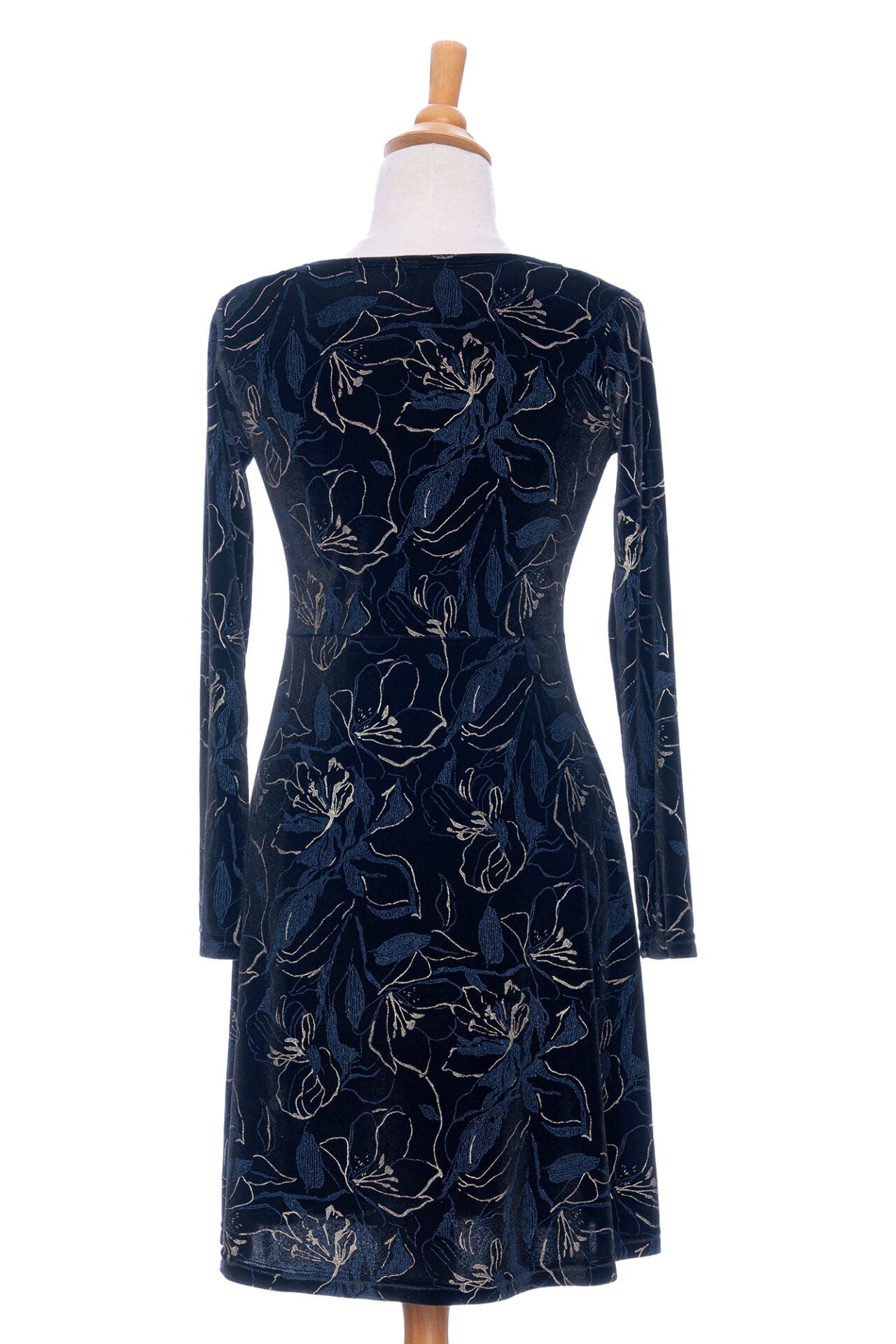 A back view of The Larix Dress by Rien ne se Perd in Black/Navy/Gold, a velvet dress with a floral pattern, a round neck, an a knee-length A-line shape, is shown on a mannequin in front of a white background. 