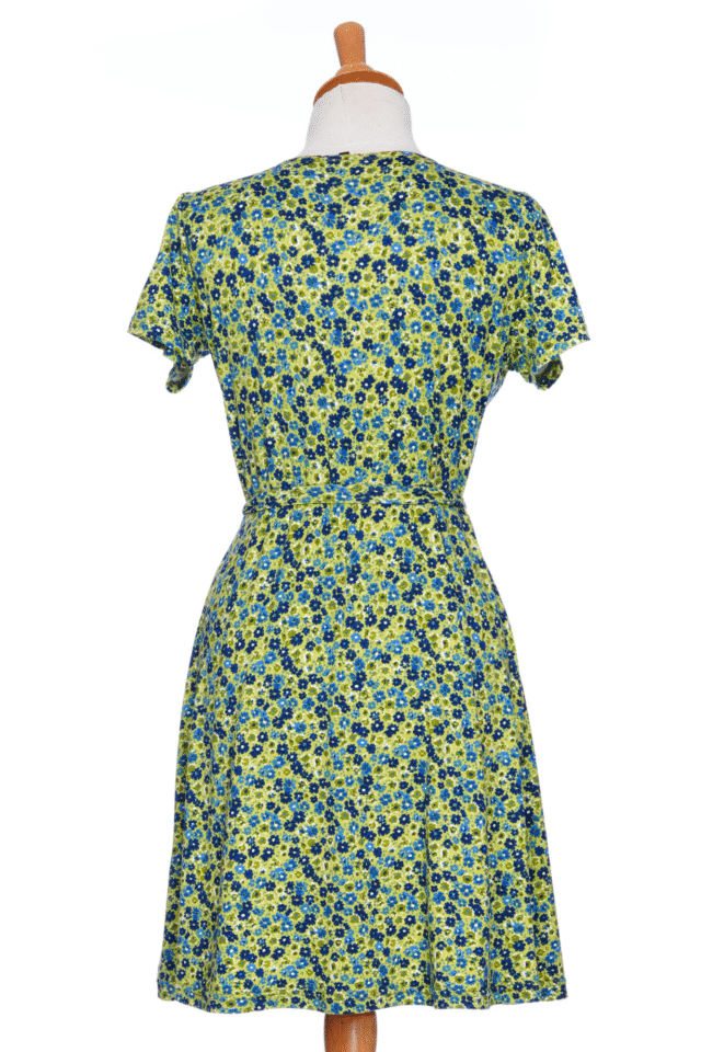 A back view of the Margarita Dress by Rien ne se Perd in Blue/Green floral print, with a faux wrap neckline, short sleeves, and short a-line skirt, is shown on a mannequin in front of a white background.