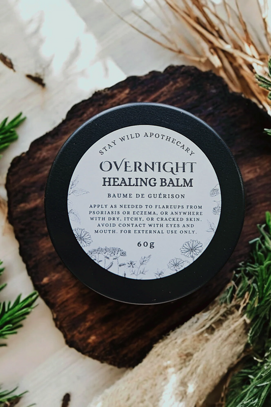 An 'Overnight Healing Balm' container by Stay Wild Apothecary is shown on a wooden surface with natural elements