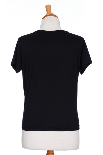 A back view of the Tropical T-shirt from Rien ne se Perd in black, with a wide neck, hi-low hemline, and tie detail at the front, is shown on a mannequin in front of a white background. 