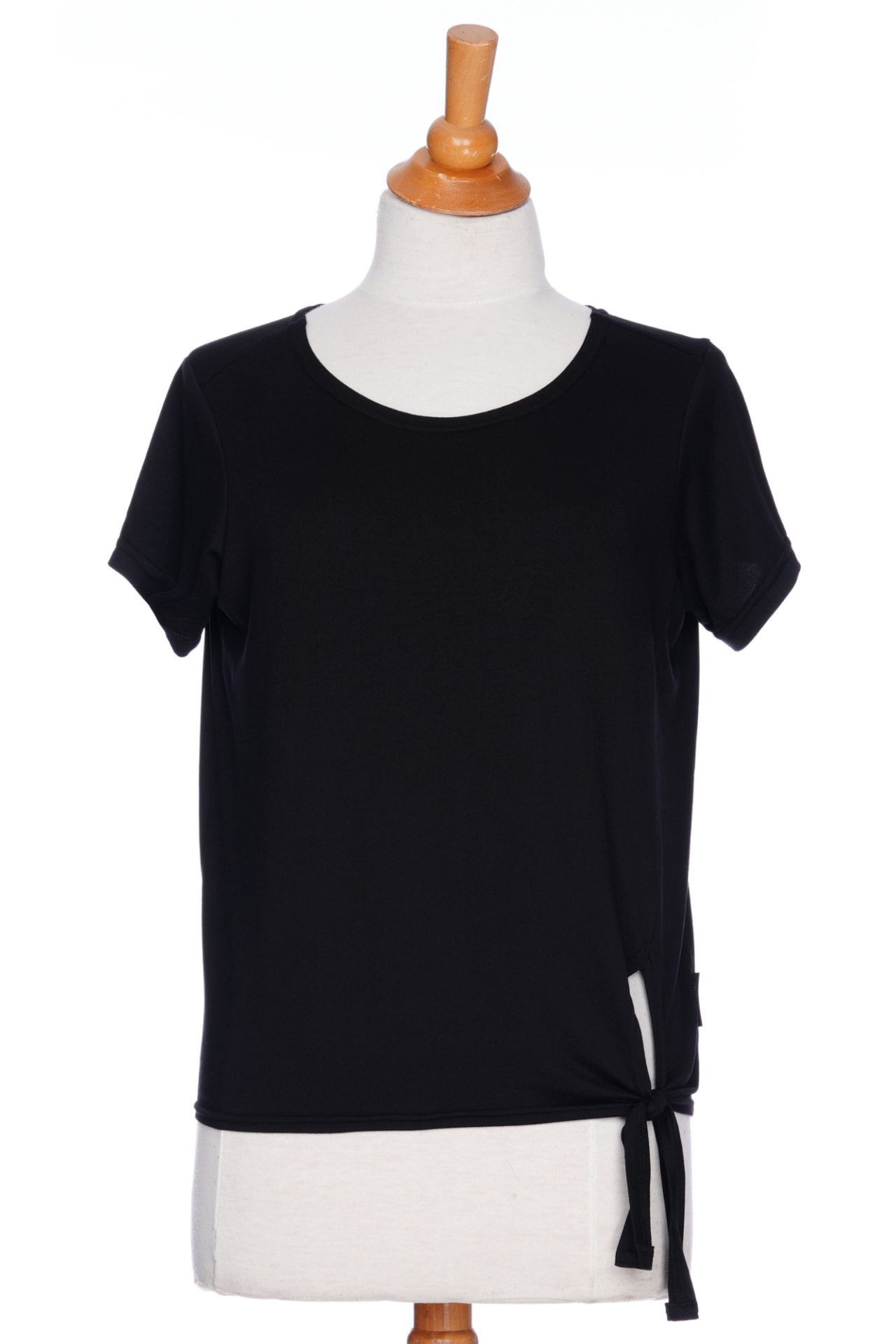 The Tropical T-shirt from Rien ne se Perd in black, with a wide neck, hi-low hemline, and tie detail at the front, is shown on a mannequin in front of a white background. 