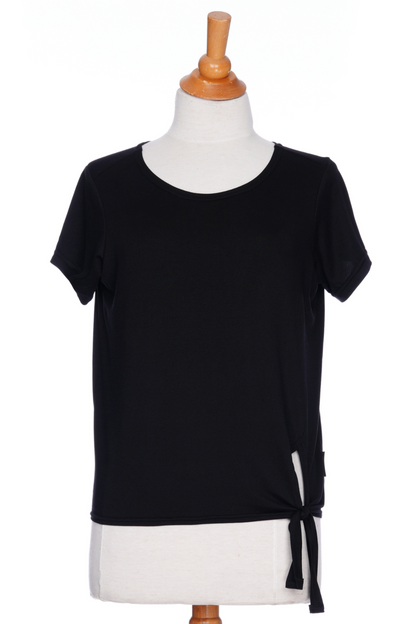 The Tropical T-shirt from Rien ne se Perd in black, with a wide neck, hi-low hemline, and tie detail at the front, is shown on a mannequin in front of a white background. 