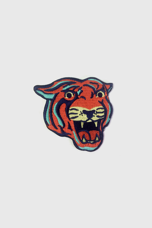 The Tiger embroidered patch from Badaboöm Studio, with orange-red fur, black stripes, and teal and cream accents, centred on a light grey background.