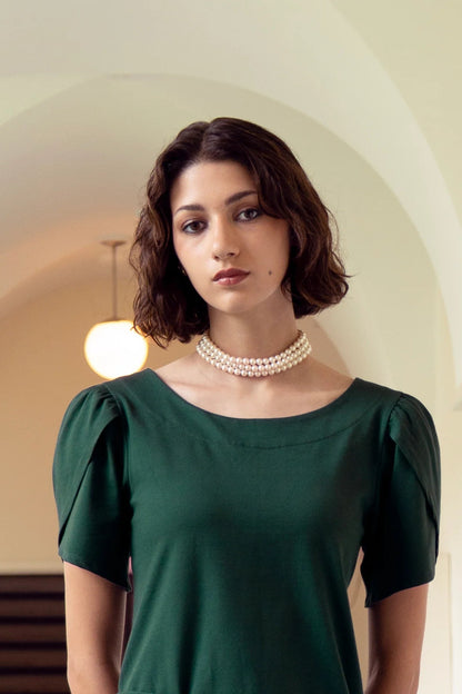 A woman wearing the Tanzania Tulip Top by Eve Lavoie in Green, with a round neck and tulip sleeves. She is standing indoors. 