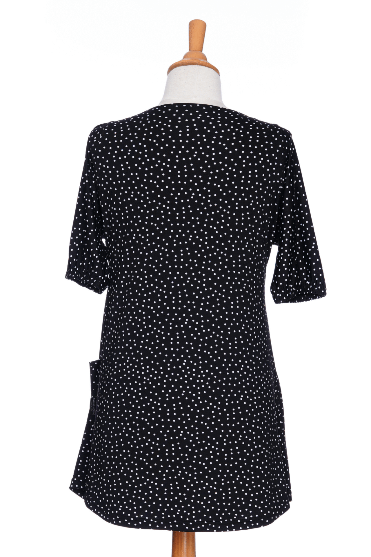A back view of the Martini Tunic from Rien ne se Perd, a black polka dot piece with full elbow length sleeves with gathered cuffs, and two patch pockets., is shown on a mannequin against a white background. 